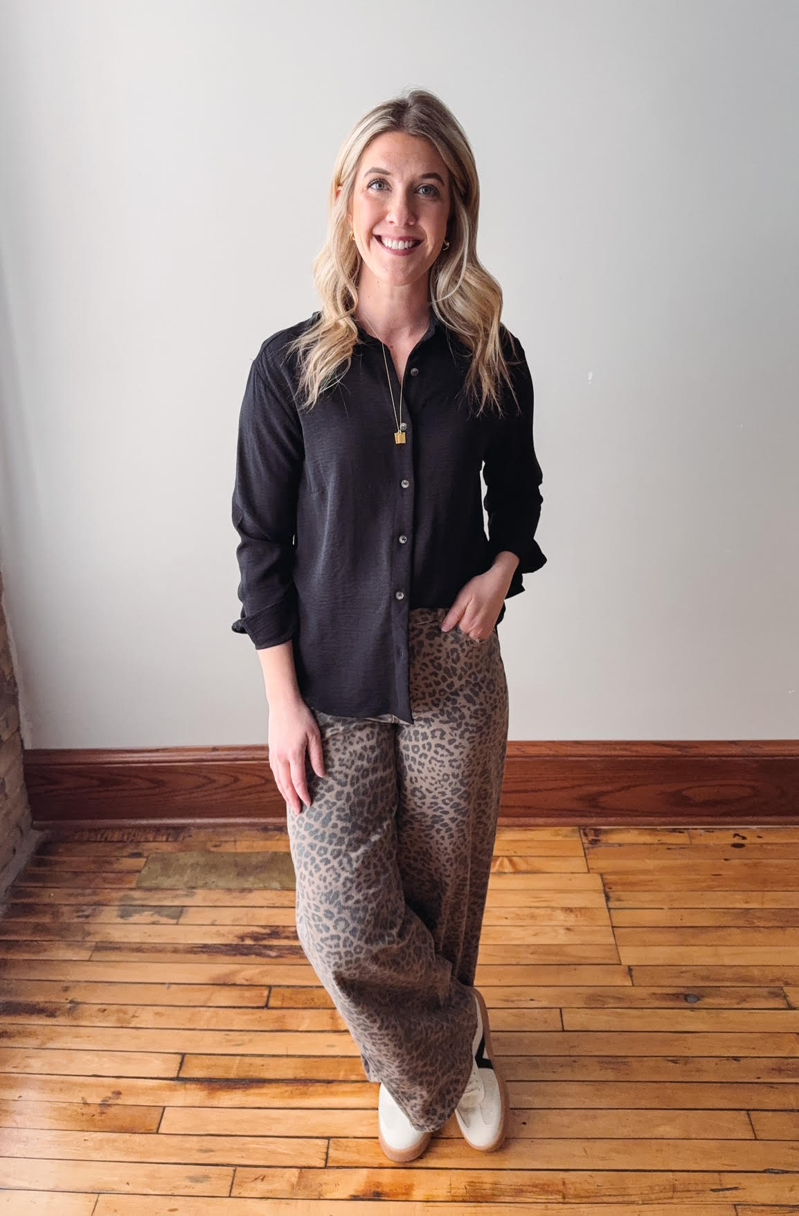 Woman wearing a black shirt and leopard print pants standing on a wooden floor.