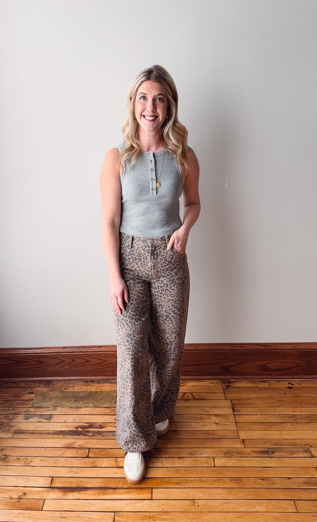 Woman wearing a sleeveless top and patterned pants standing on a wooden floor.