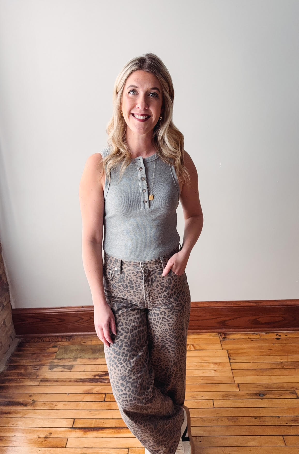 Woman wearing a sleeveless top and patterned pants standing in a room with wooden flooring and white walls.