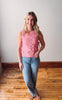 Woman wearing a pink sleeveless sweater and blue jeans standing on a wooden floor.