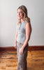 Woman wearing a gray sleeveless top and patterned pants standing on a wooden floor.