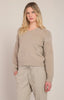 Woman wearing a beige sweater and pants against a plain background