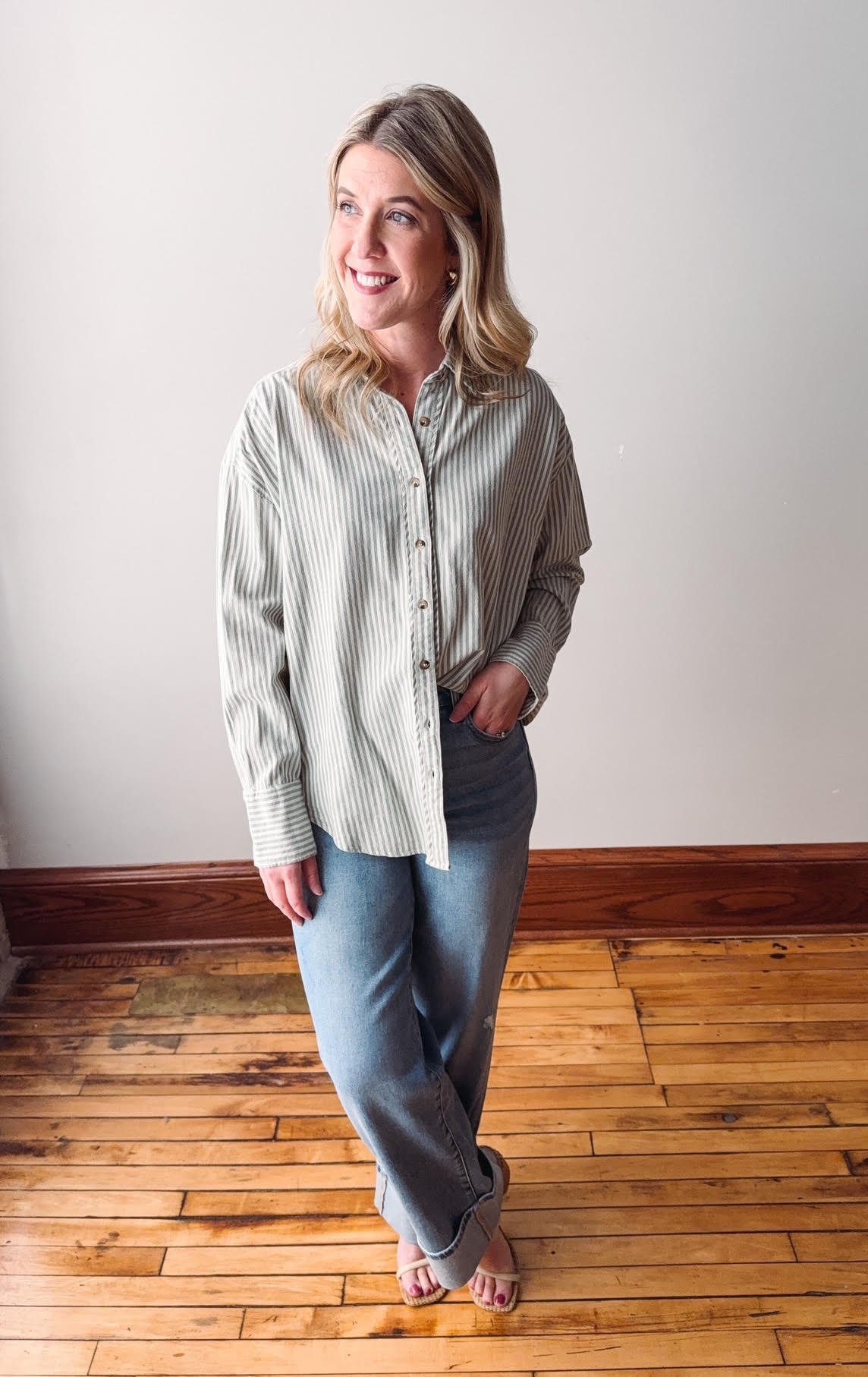 Woman wearing a striped shirt and jeans standing on a wooden floor.