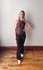 Woman in brown tank top and black leggings standing on a wooden floor with a white wall background
