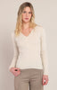 Woman wearing a beige sweater and beige pants against a plain background