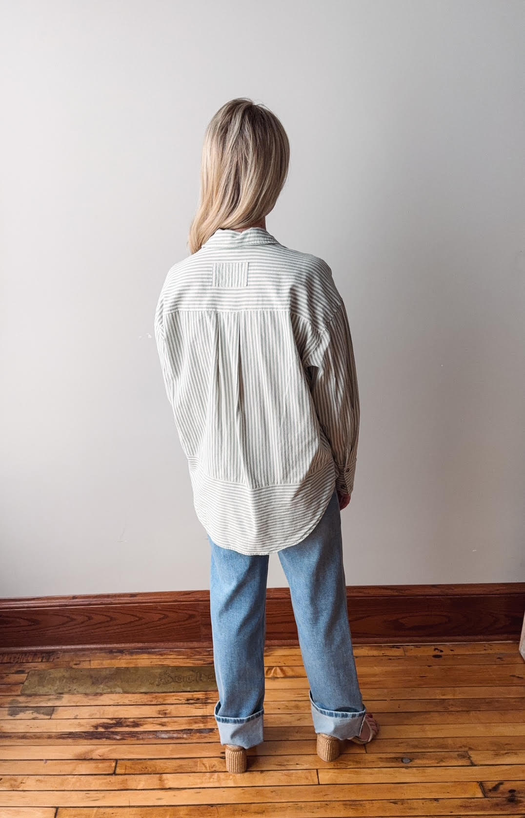 Person wearing a light-colored shirt and jeans standing against a plain wall.