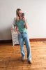 Woman taking a mirror selfie wearing a green t-shirt and blue jeans in a room with wooden flooring.