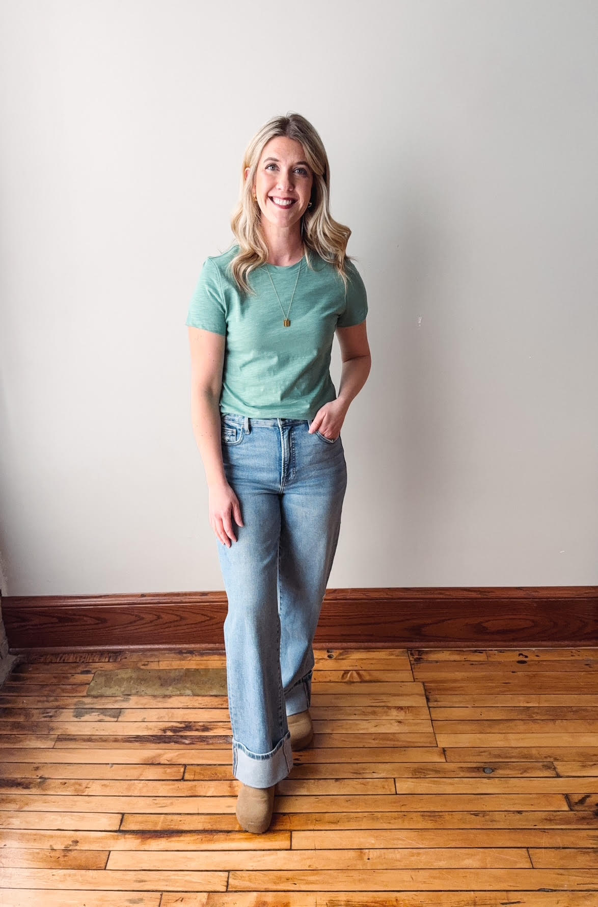 Woman wearing a green t-shirt and blue jeans standing on a wooden floor.