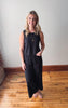 Woman wearing a black sleeveless dress standing on a wooden floor.