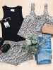 Collection of clothing and accessories including a black tank top, floral shorts, jeans, and sunglasses on a light wooden surface.
