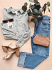 Striped shirt, jeans, sunglasses, and sandals arranged on a light surface with eucalyptus leaves.