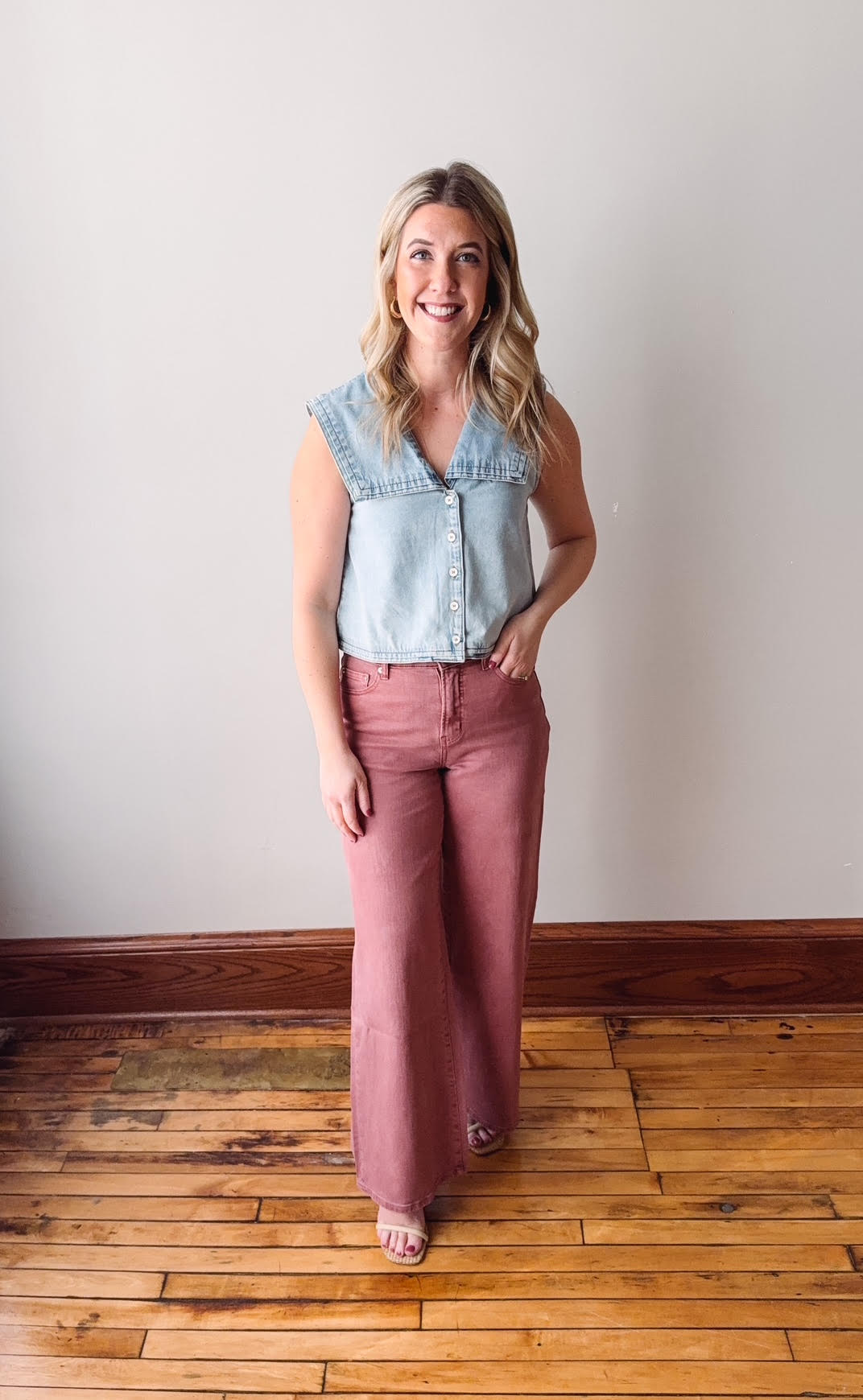 Woman wearing a denim sleeveless top and pink pants standing on a wooden floor.