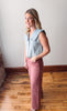 Woman wearing a light blue sleeveless denim jacket and pink pants standing on a wooden floor.