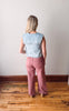 Person wearing a light blue denim top and pink pants standing on a wooden floor with a white wall background
