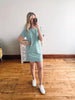 Woman taking a mirror selfie wearing a striped dress and white sneakers in a room with wooden flooring.