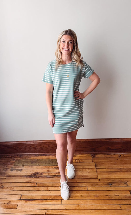 Woman wearing a light blue striped dress standing on a wooden floor with a white wall background