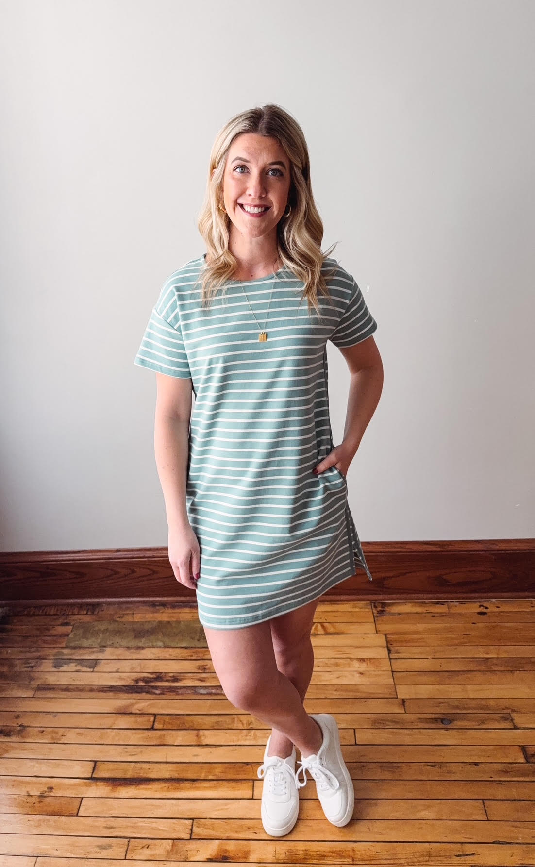 Woman wearing a striped dress standing on a wooden floor with a white wall background