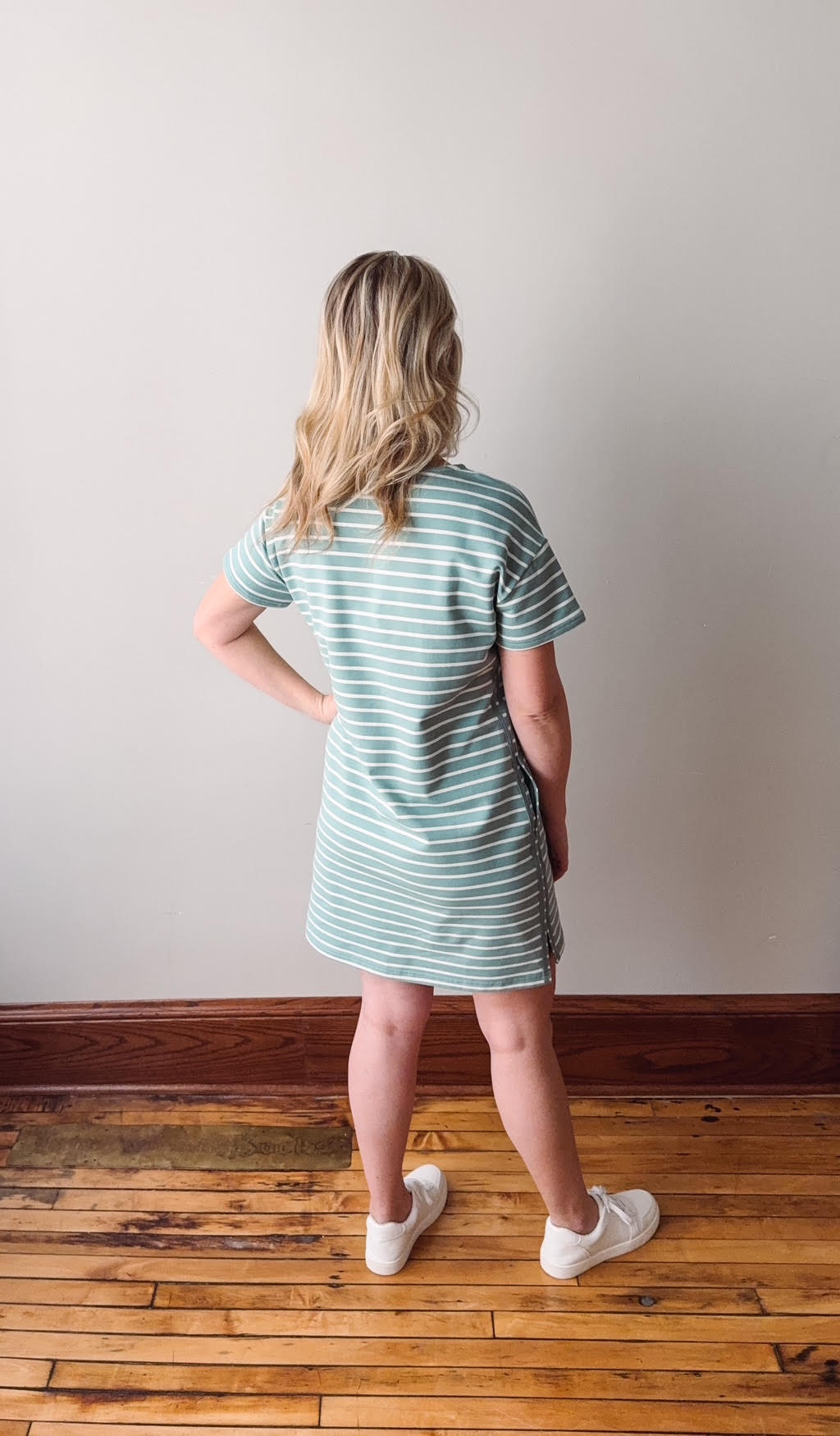 Woman wearing a striped dress standing on a wooden floor with a plain wall background