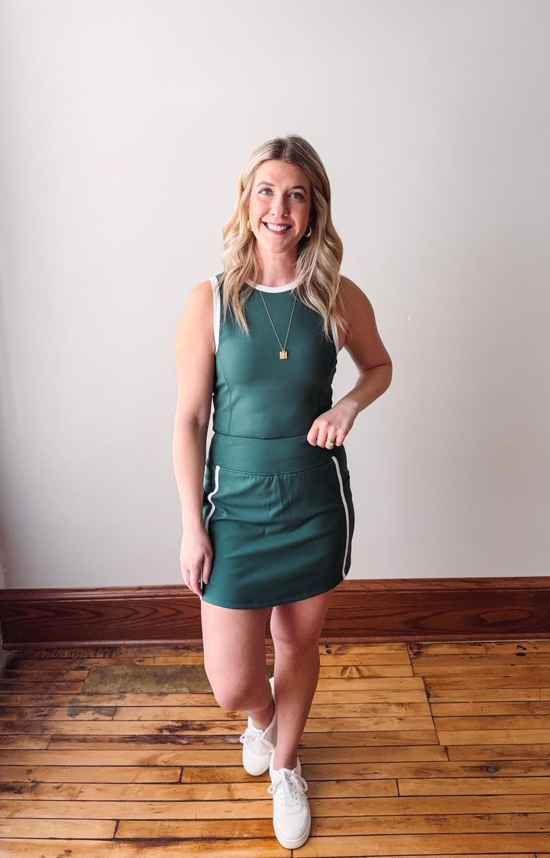 Woman wearing a green dress standing on a wooden floor with a white wall background