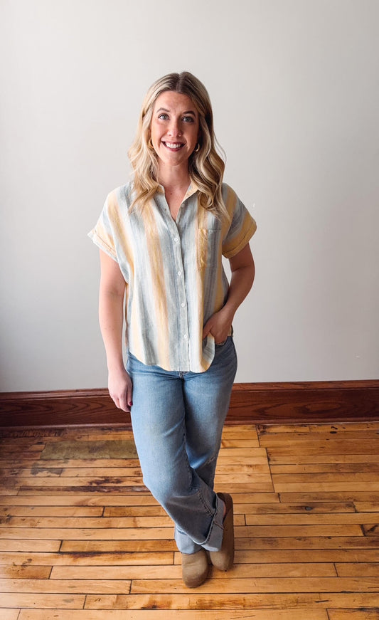 Woman wearing a striped shirt and jeans standing on a wooden floor with a white wall background