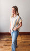Woman wearing a striped shirt and jeans standing on a wooden floor with a white wall background