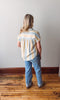 Person wearing a striped shirt and jeans standing on a wooden floor against a white wall.