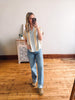Person taking a mirror selfie wearing a striped shirt and jeans in a room with wooden flooring.