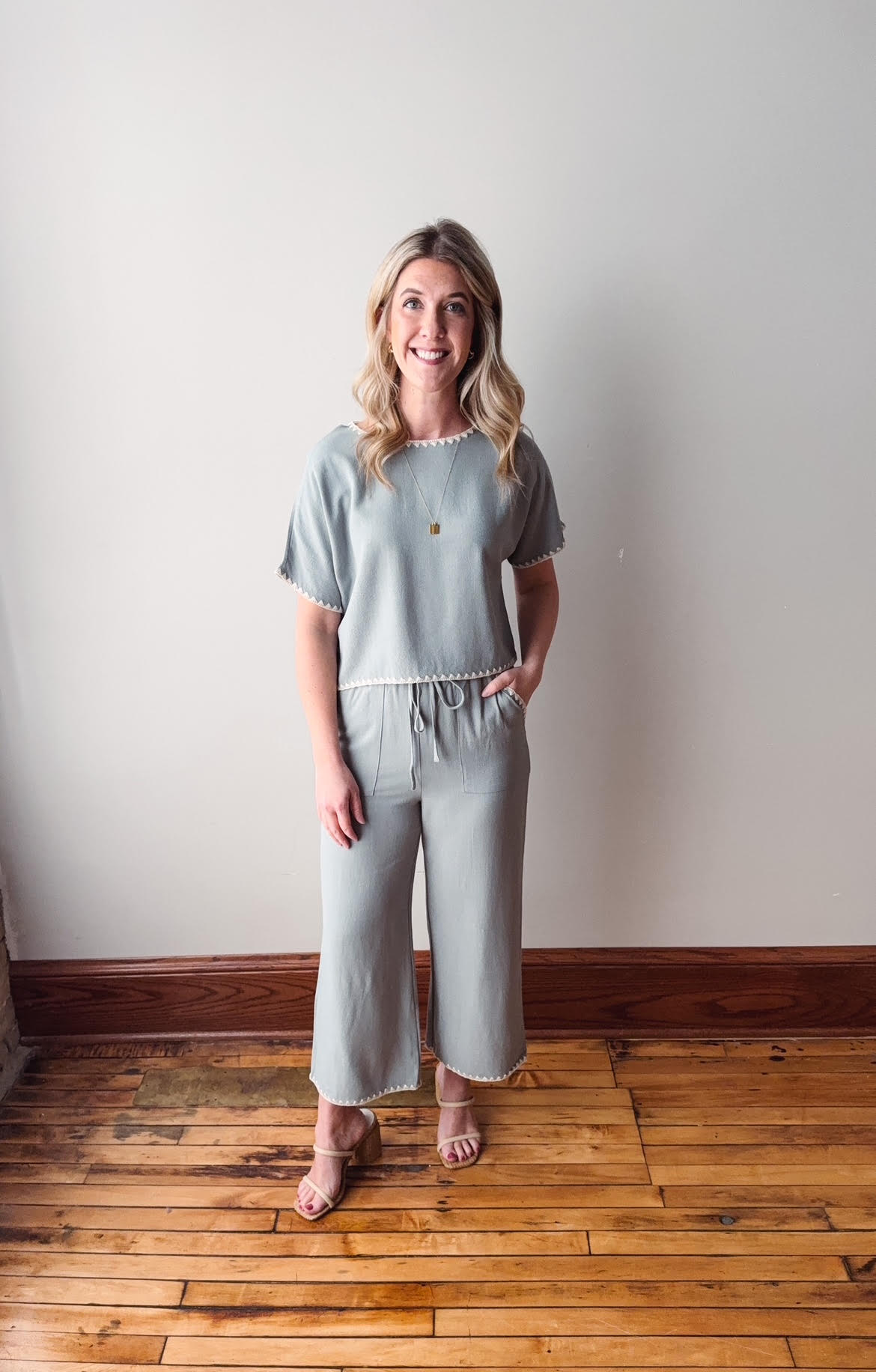 Woman wearing a light blue outfit standing on a wooden floor against a white wall.