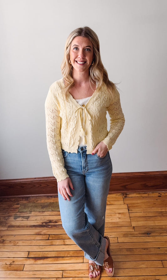 Woman wearing a yellow cardigan and blue jeans standing on a wooden floor.