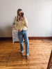 Woman taking a mirror selfie wearing a yellow cardigan and blue jeans in a room with wooden flooring.