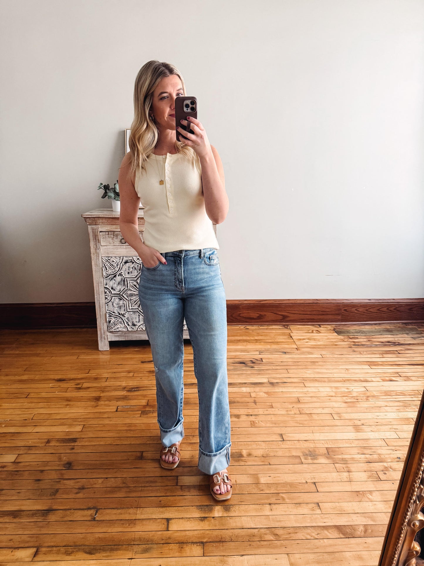 Woman taking a mirror selfie wearing a white top and blue jeans in a room with wooden flooring.