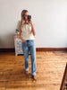Woman taking a mirror selfie wearing a white top and blue jeans in a room with wooden flooring.