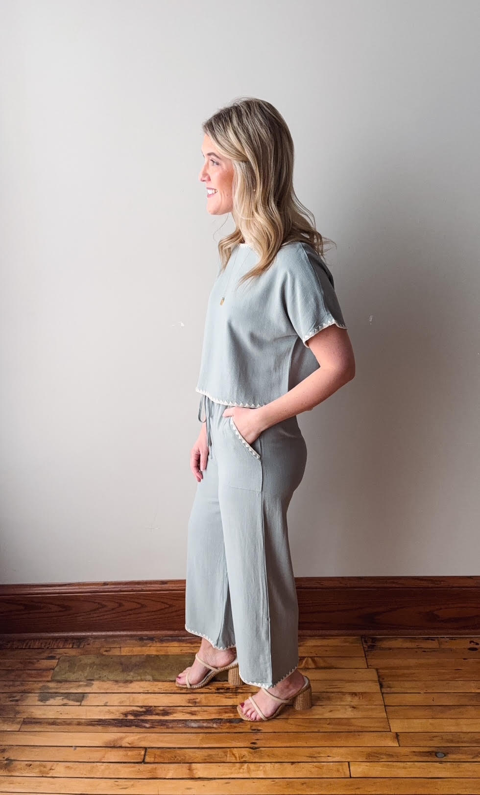 Woman wearing a light gray outfit standing against a plain wall.