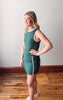 Woman wearing a green dress with white trim standing on a wooden floor.