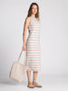 Woman wearing a striped dress holding a tote bag on a plain background