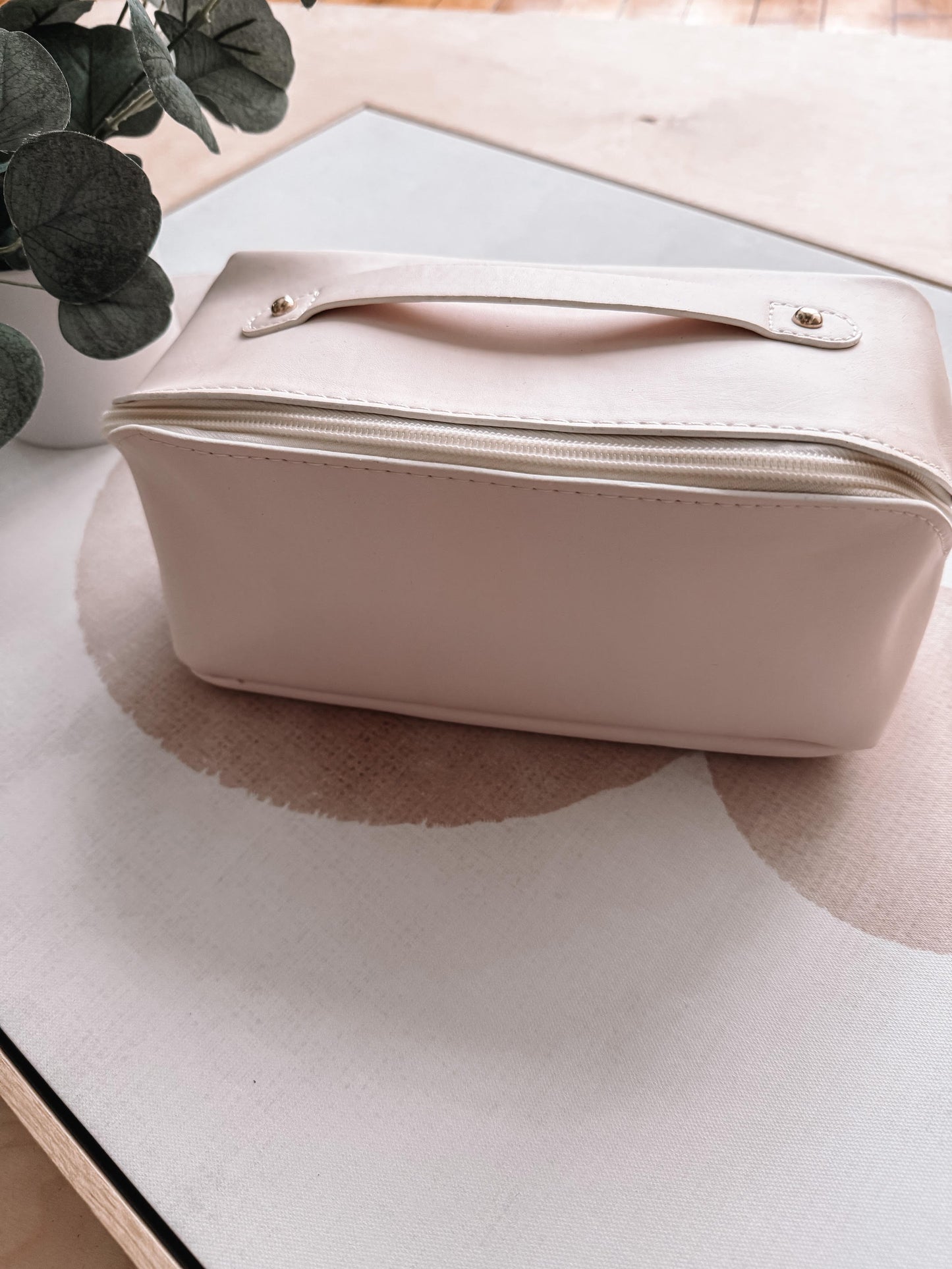 White toiletry bag on a light surface with a plant in the background
